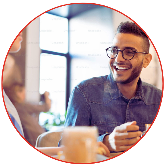 A man with glasses and a bright smile sits at a table.