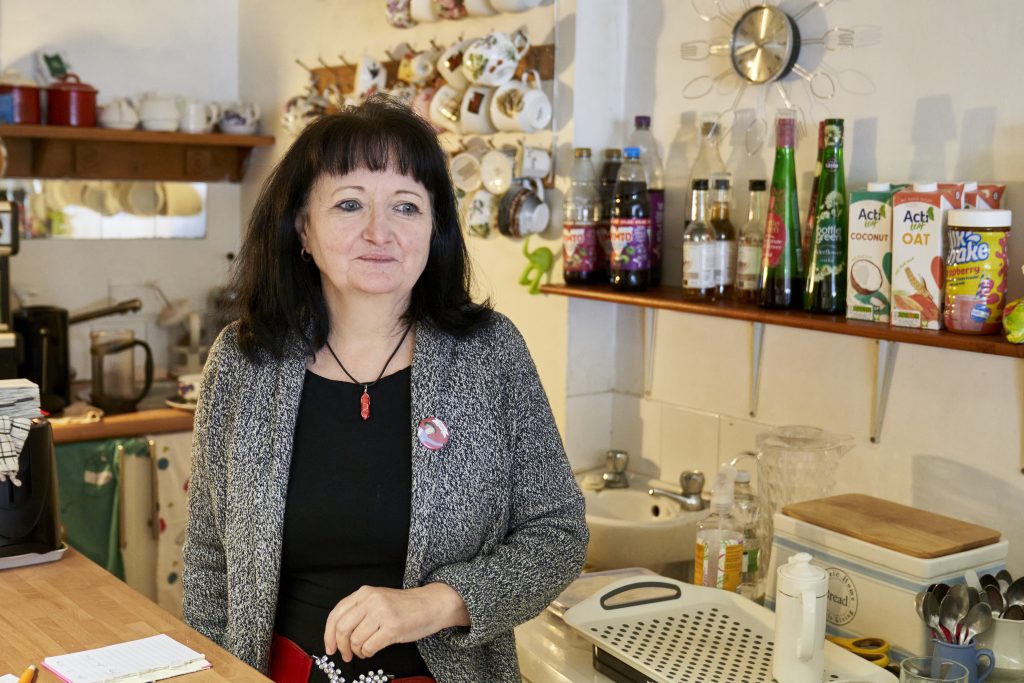 A woman smiles while standing at a counter filled with a variety of delicious food items.