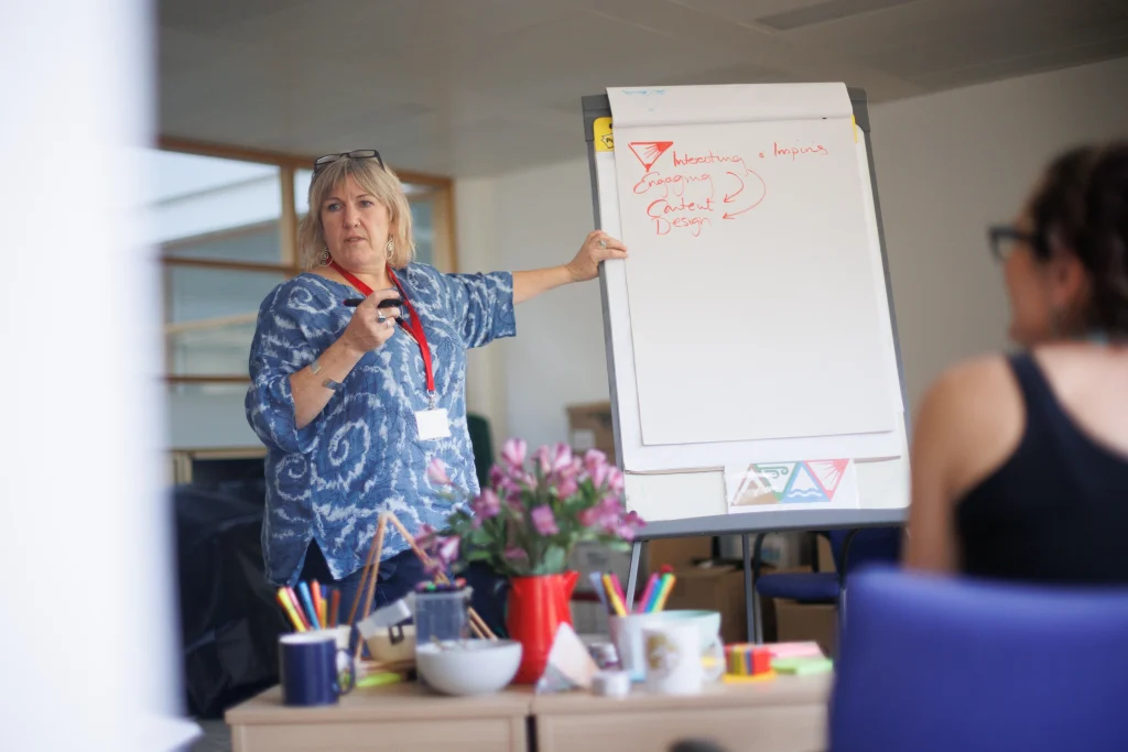 A woman confidently presents to an engaged audience, sharing her ideas and insights in a professional setting.